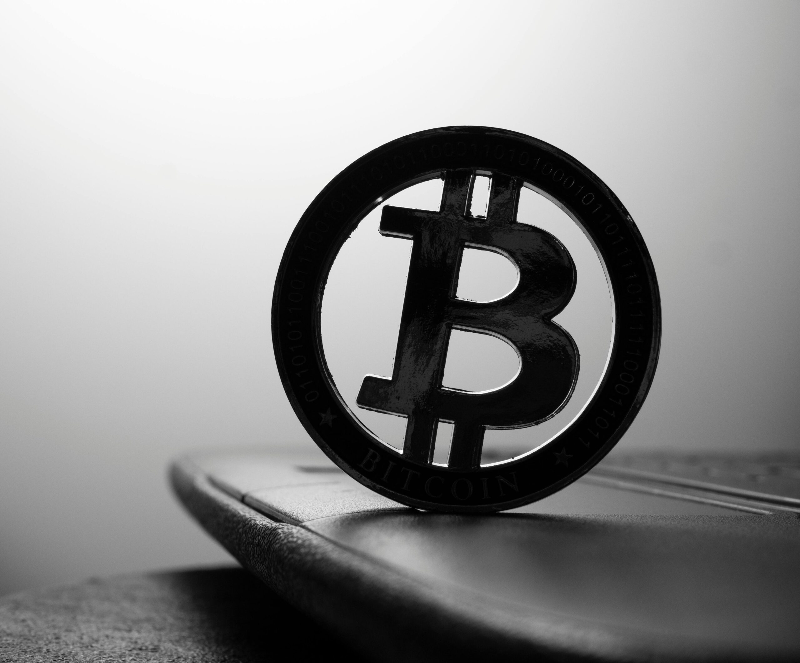 A close-up black and white image of a Bitcoin symbol standing on a laptop.